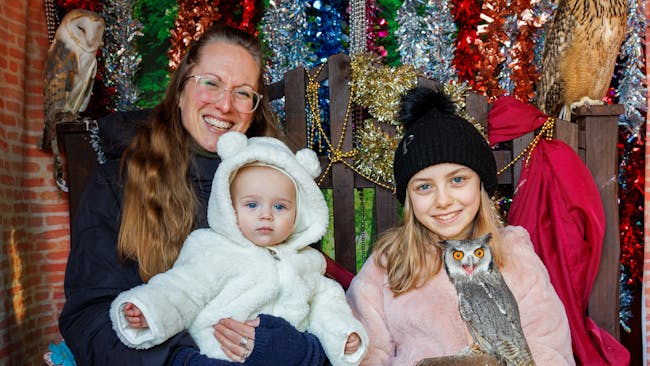 A smiling woman, a girl holding an owl, and a baby.