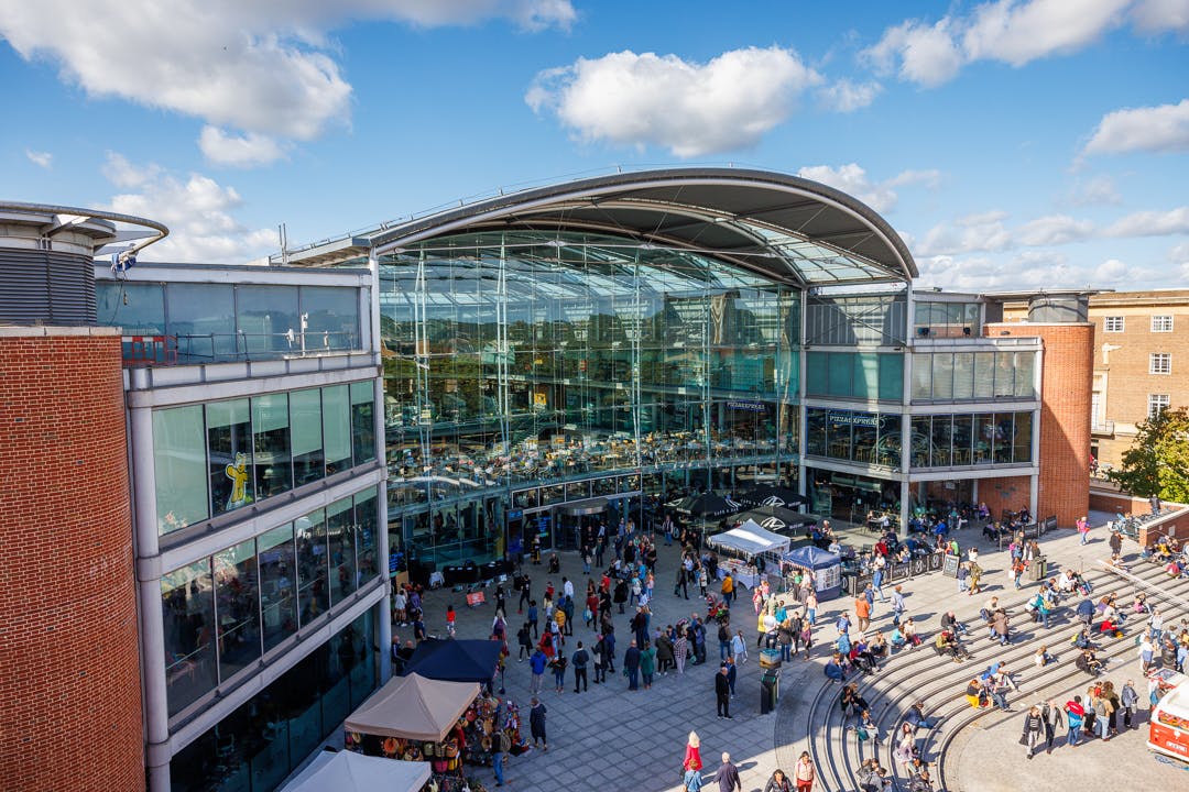 Exterior of The Forum building on a sunny day, with people and stalls