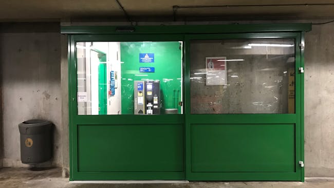 A closed green automatic door with level flooring leading to a pay machine and lift.