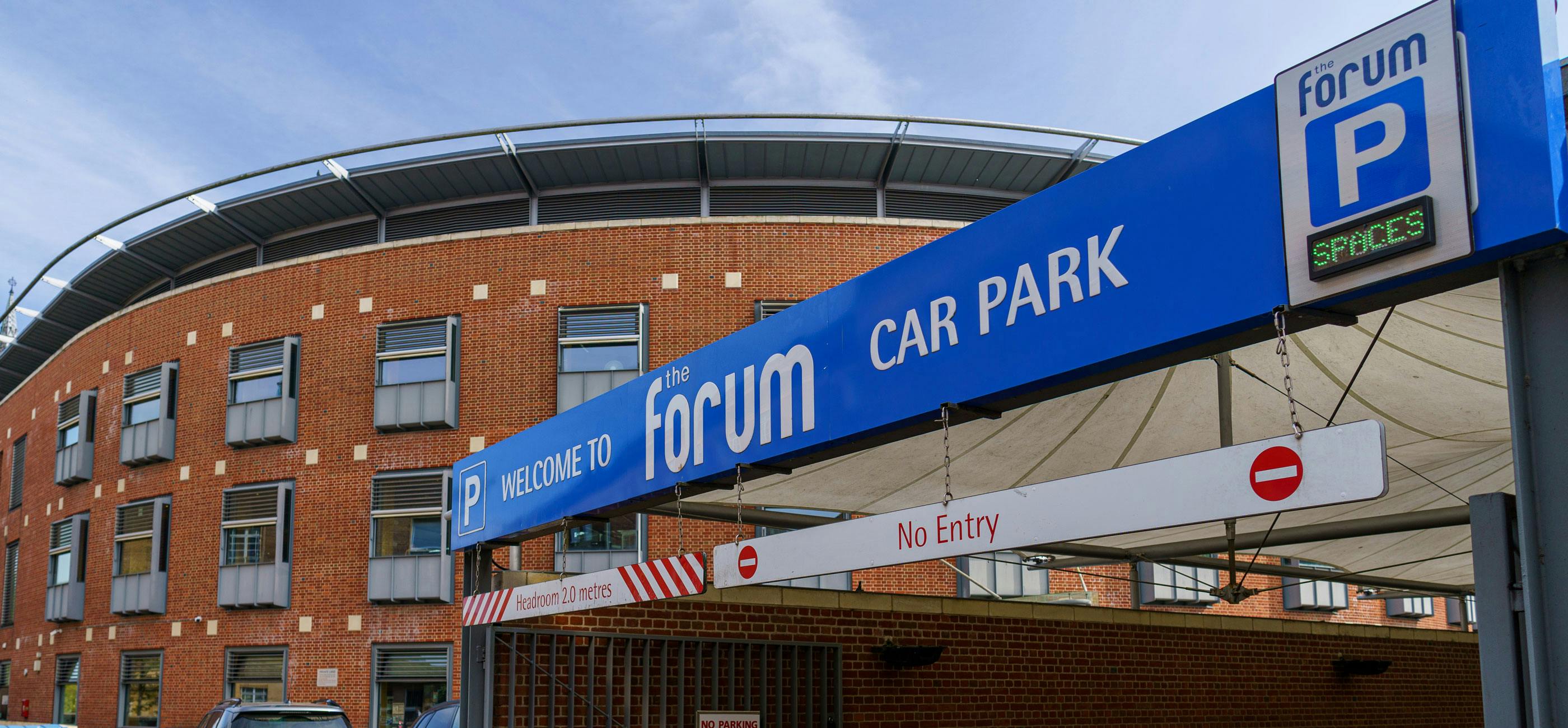 Blue car park entrance sign with The Forum building in the background.