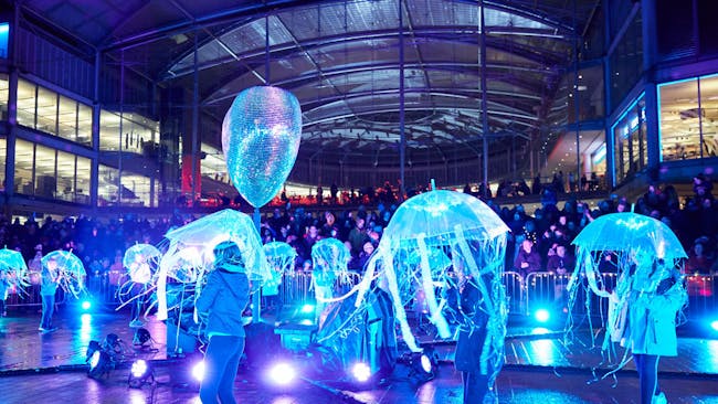 A group of children perform outside The Forum with light up umbrellas decorated to look like jellyfish.