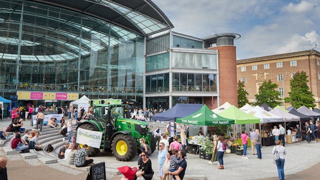 A farmers market with produce stalls and a big green tractor outside The Forum in Norwich.