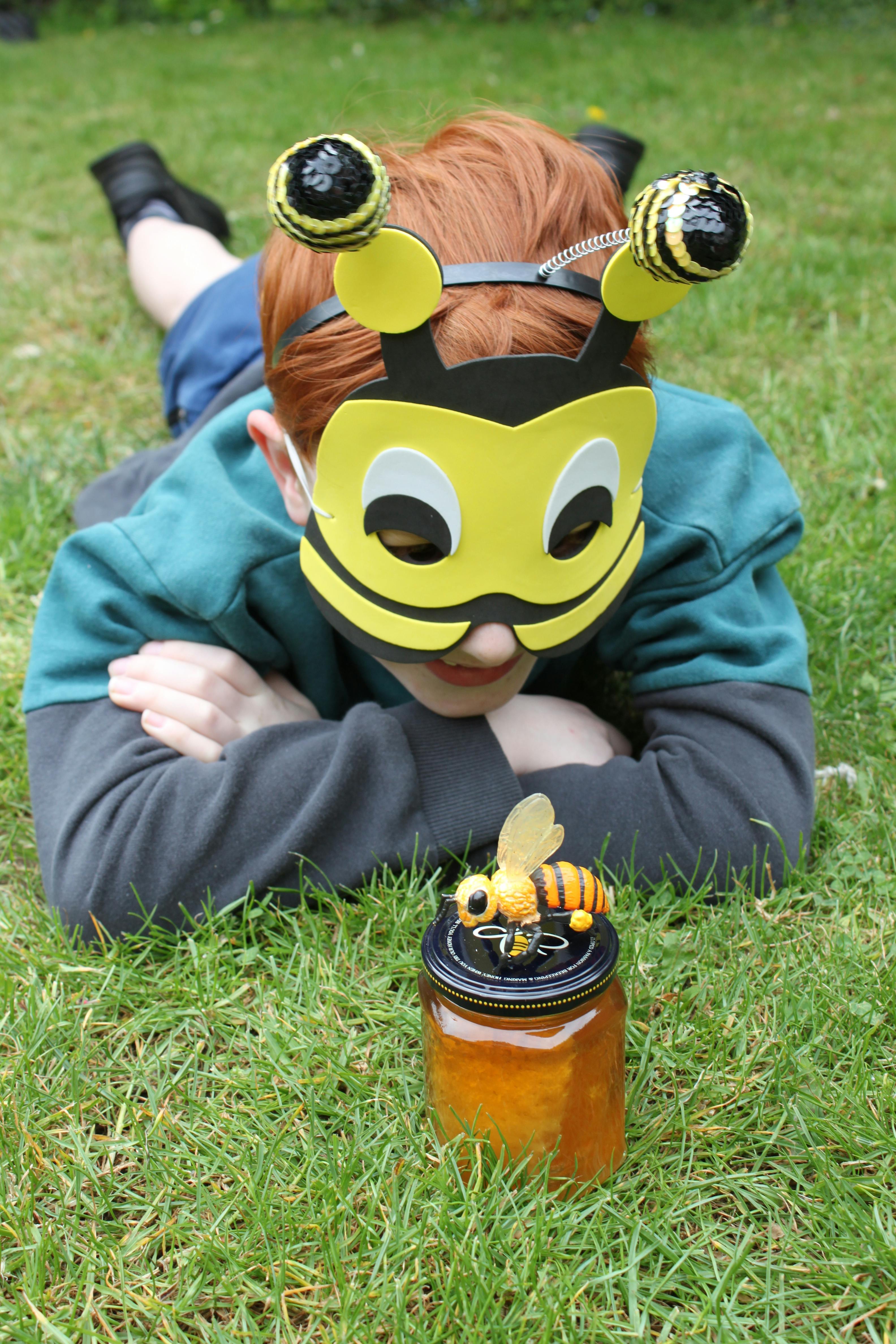 boy wearing a bee mask looking at a pot of honey