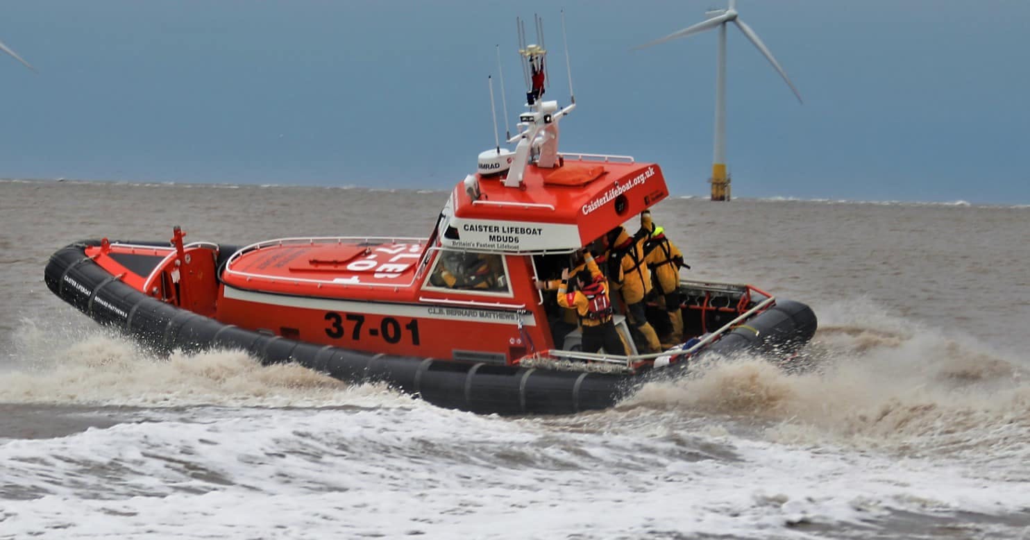 A Caister Lifeboat speeds across the Norfolk sea in front of wind turbines