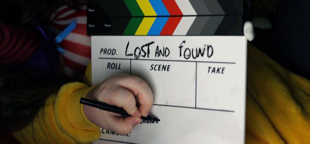 A child's hand writes on a film clapper board with the title Lost and Found on the top.