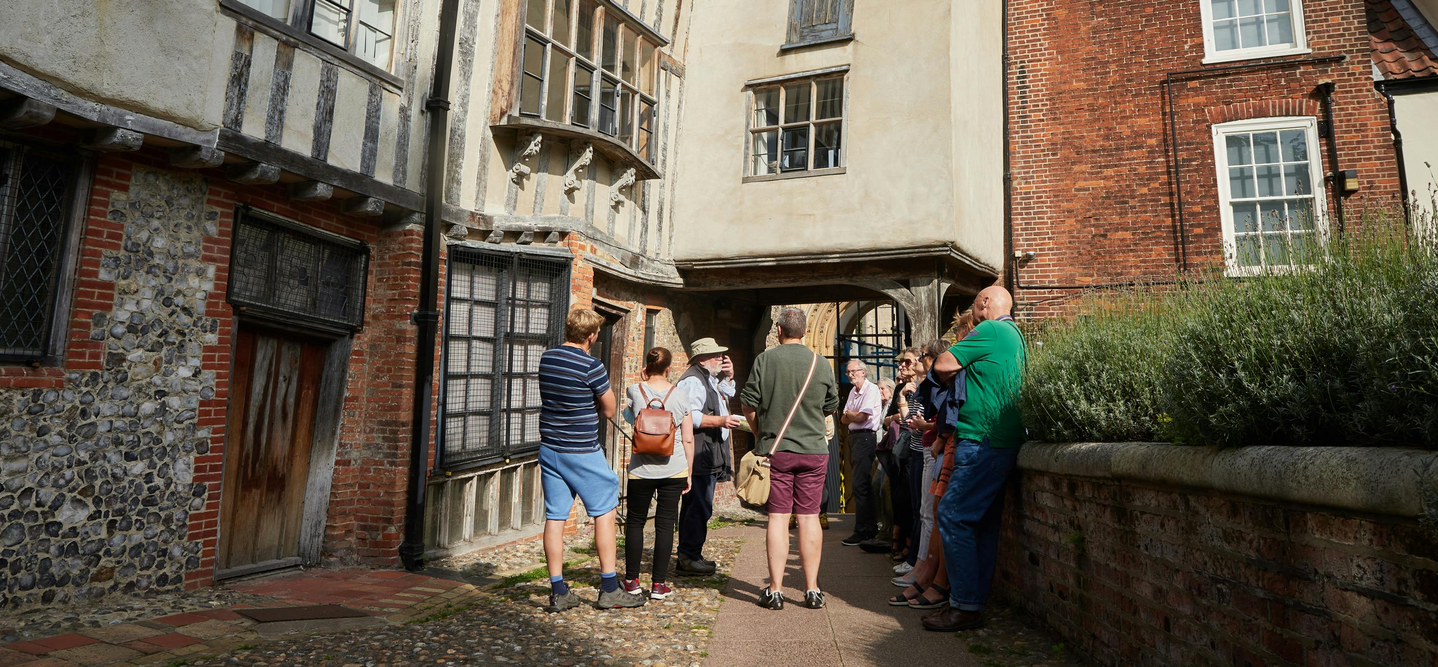 A group of people listen to a guide next to a Tudor building with wonky beams and cobbled street
