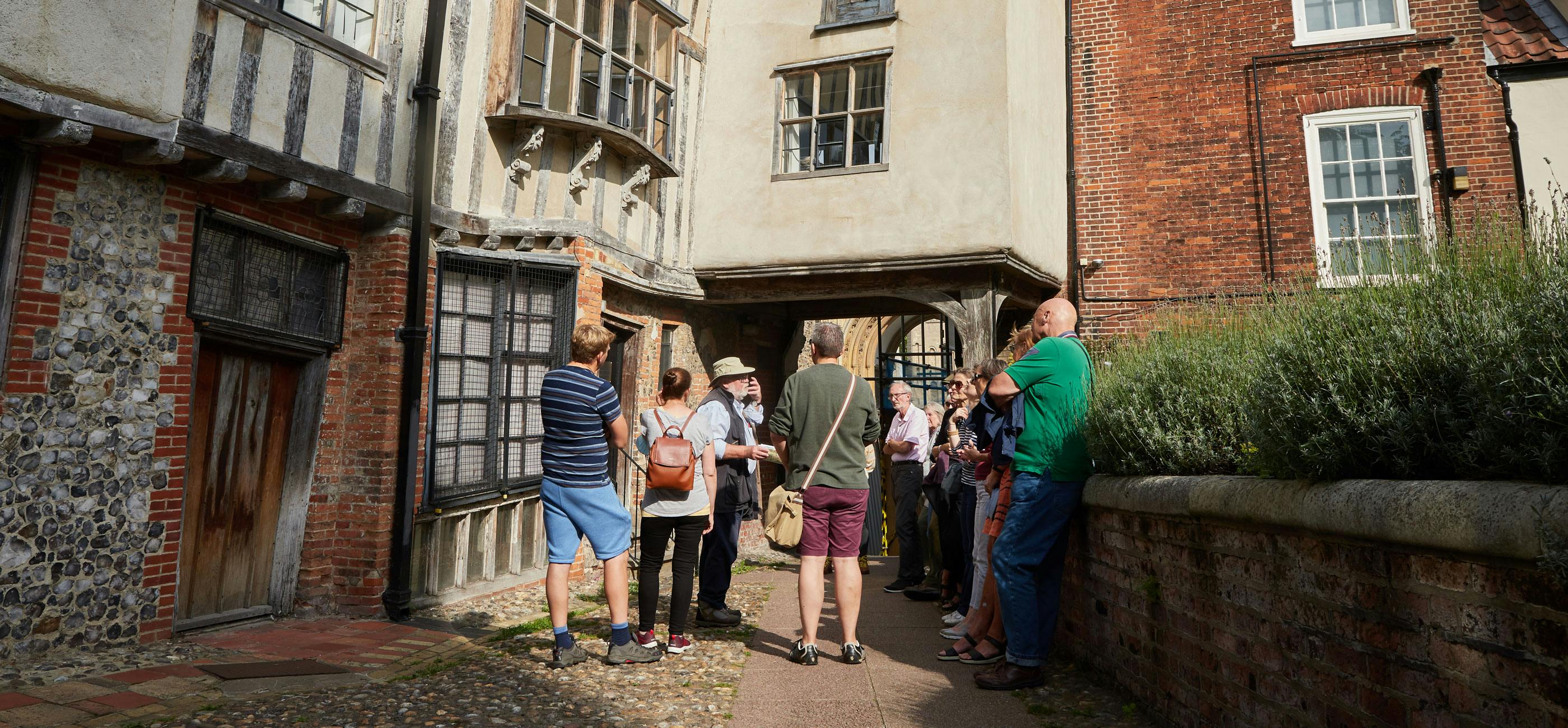 A group of people stand listening to a talk guide next to a Tudor building.