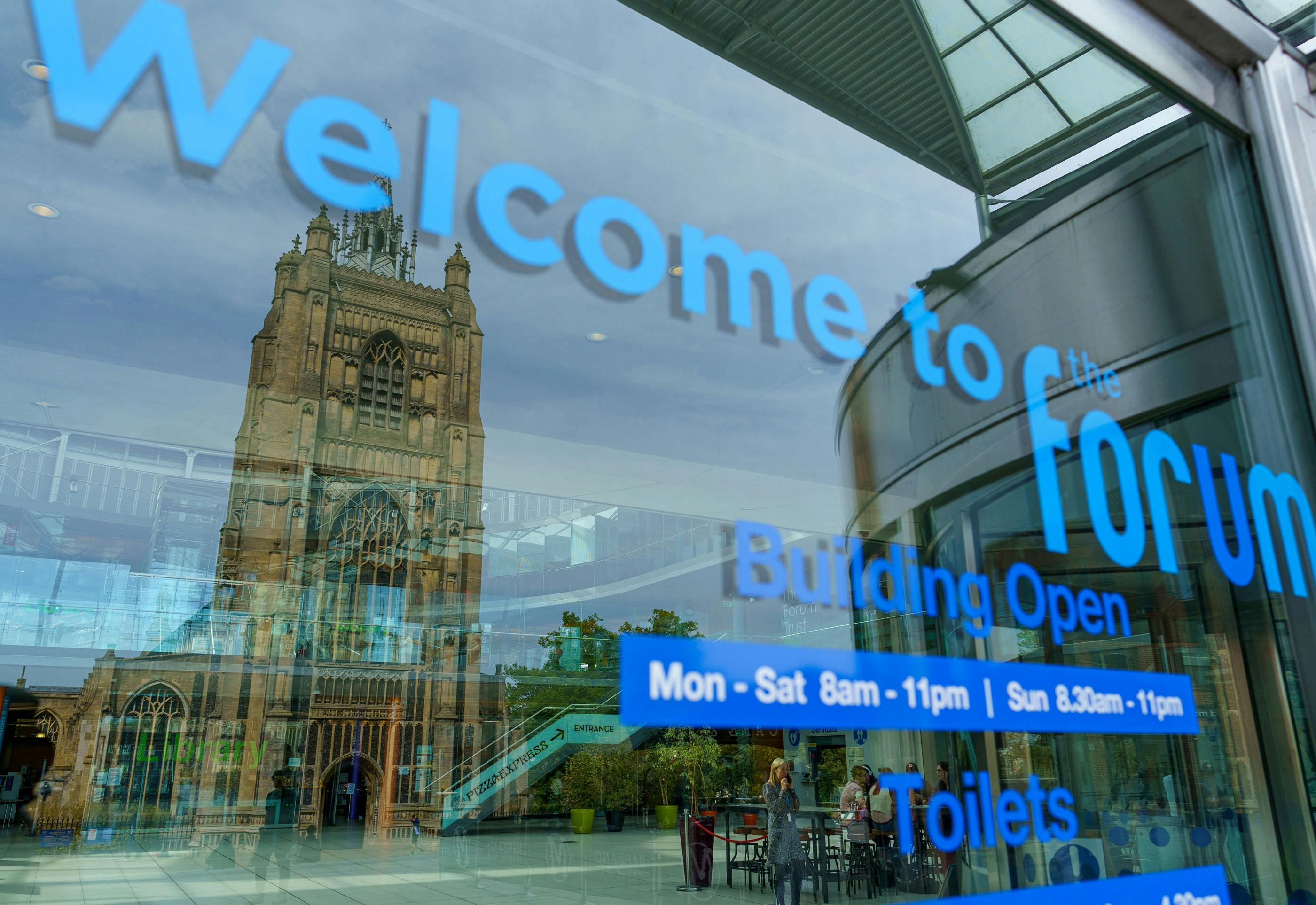 A close up of glass welcome sign at The Forum with a reflection of St Peter Mancroft church