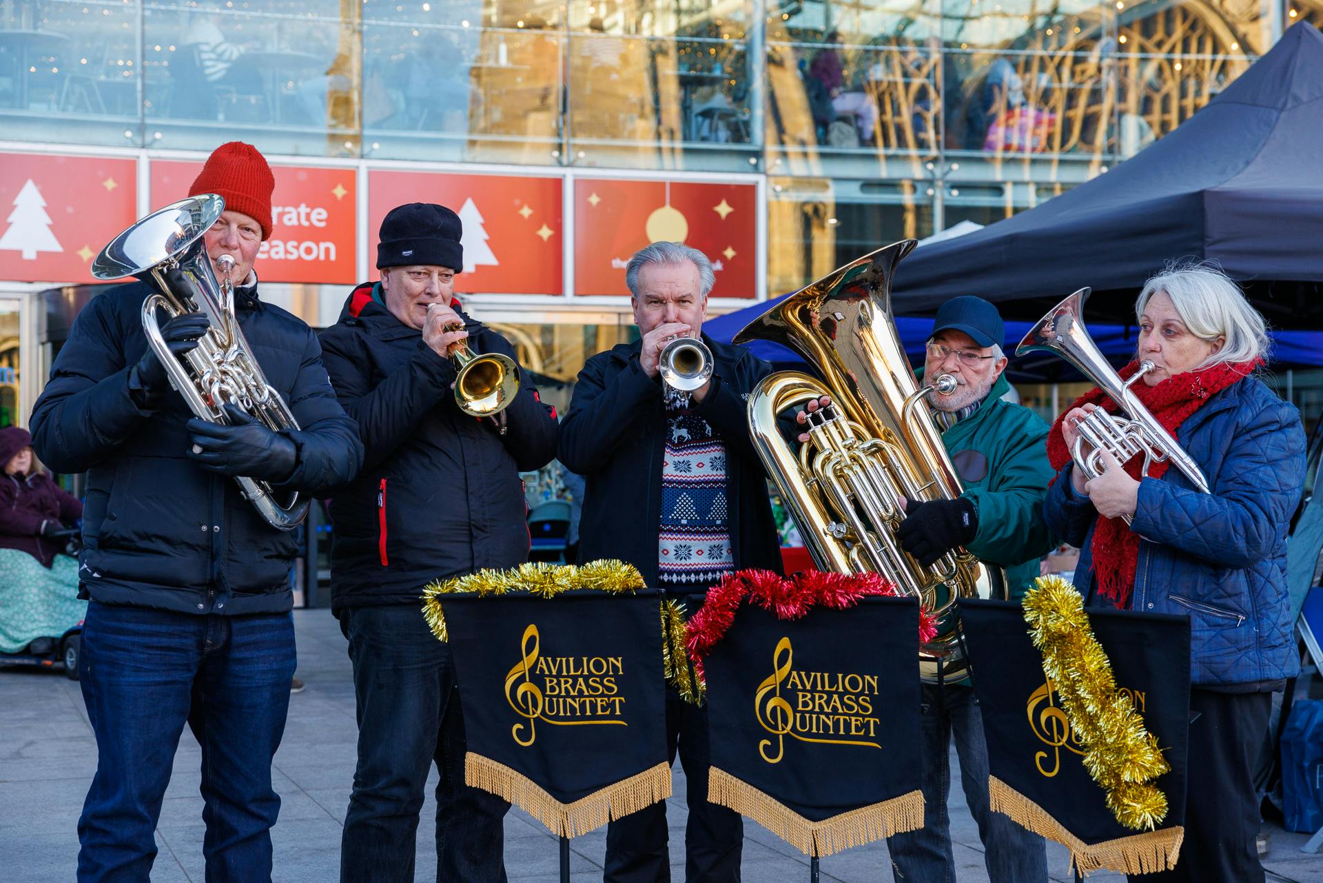 The Pavilion Brass Quintet play instruments outside The Forum with tinsel on their music stands