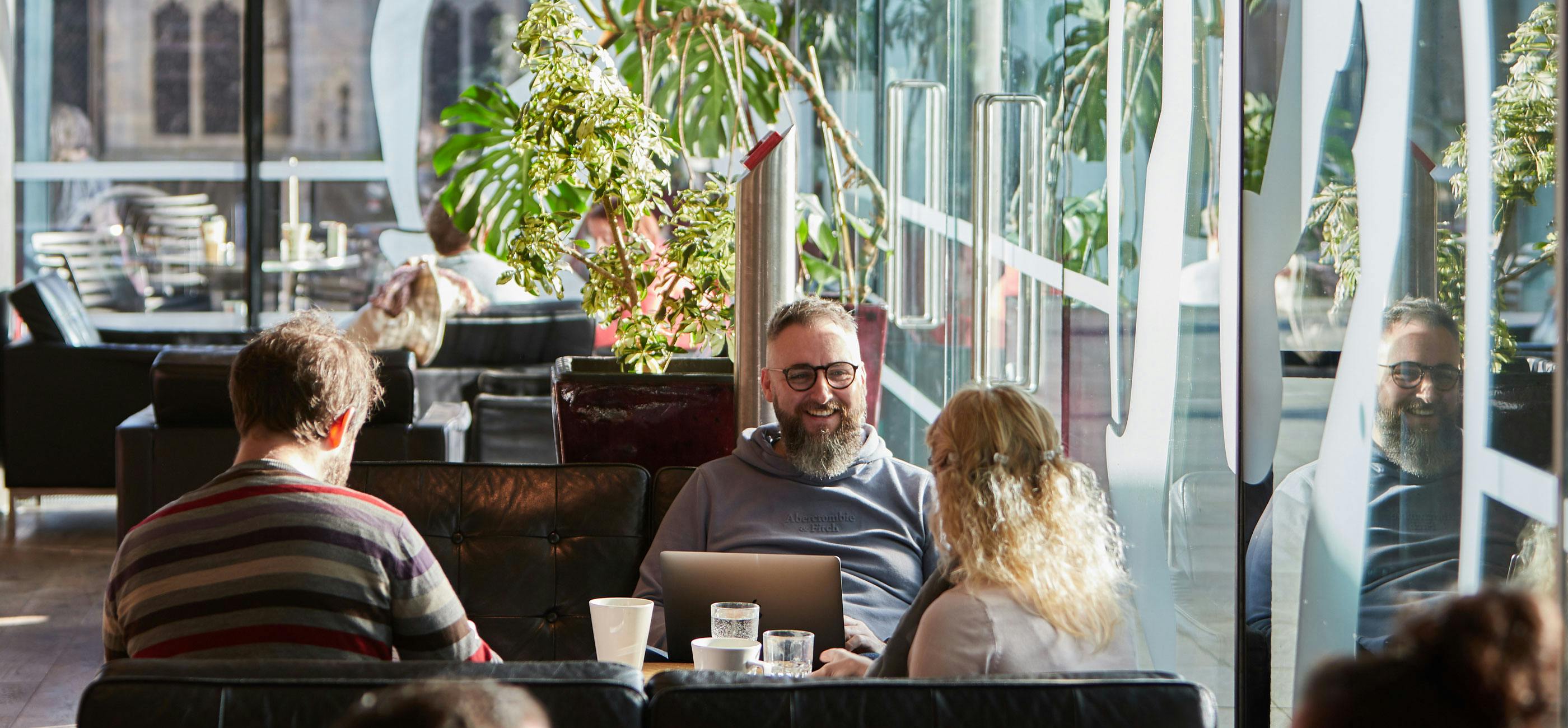 A group of friends sit in a light filled café having coffee and smiling.