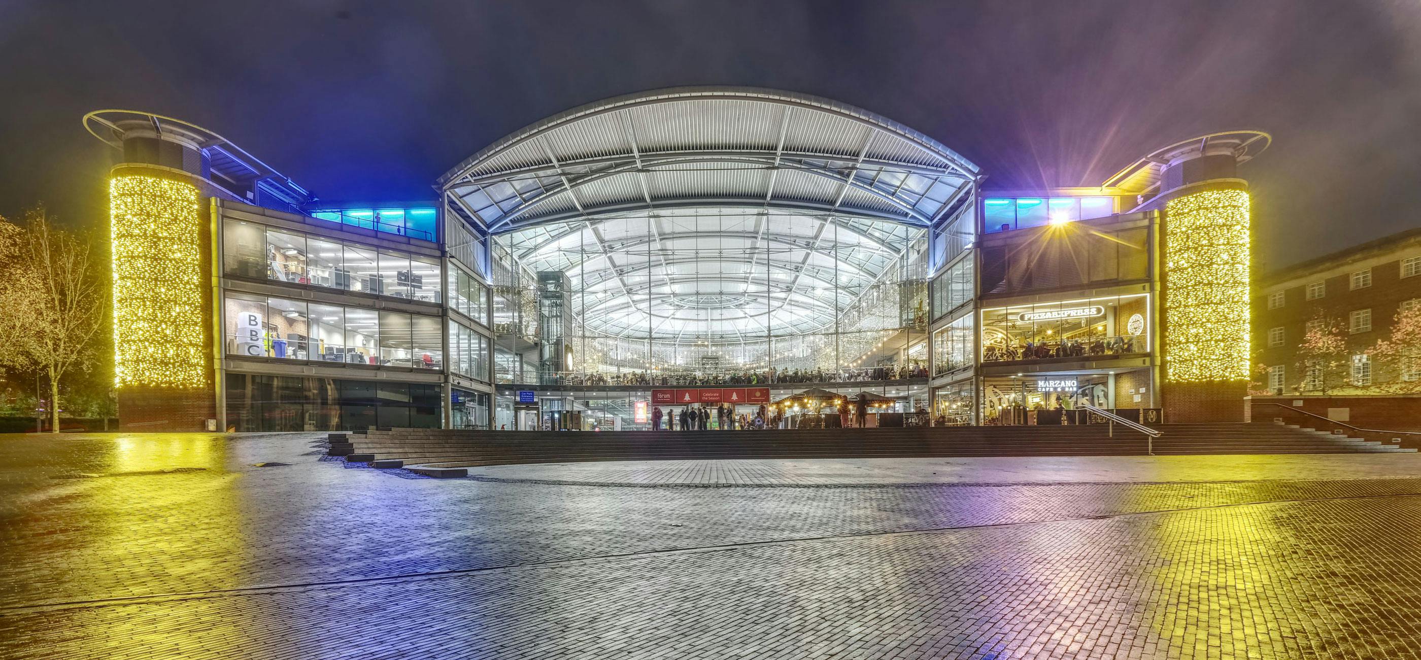 The Forum in Norwich, a large glass fronted building with fairy lights sparkling on the inside and outside at night.