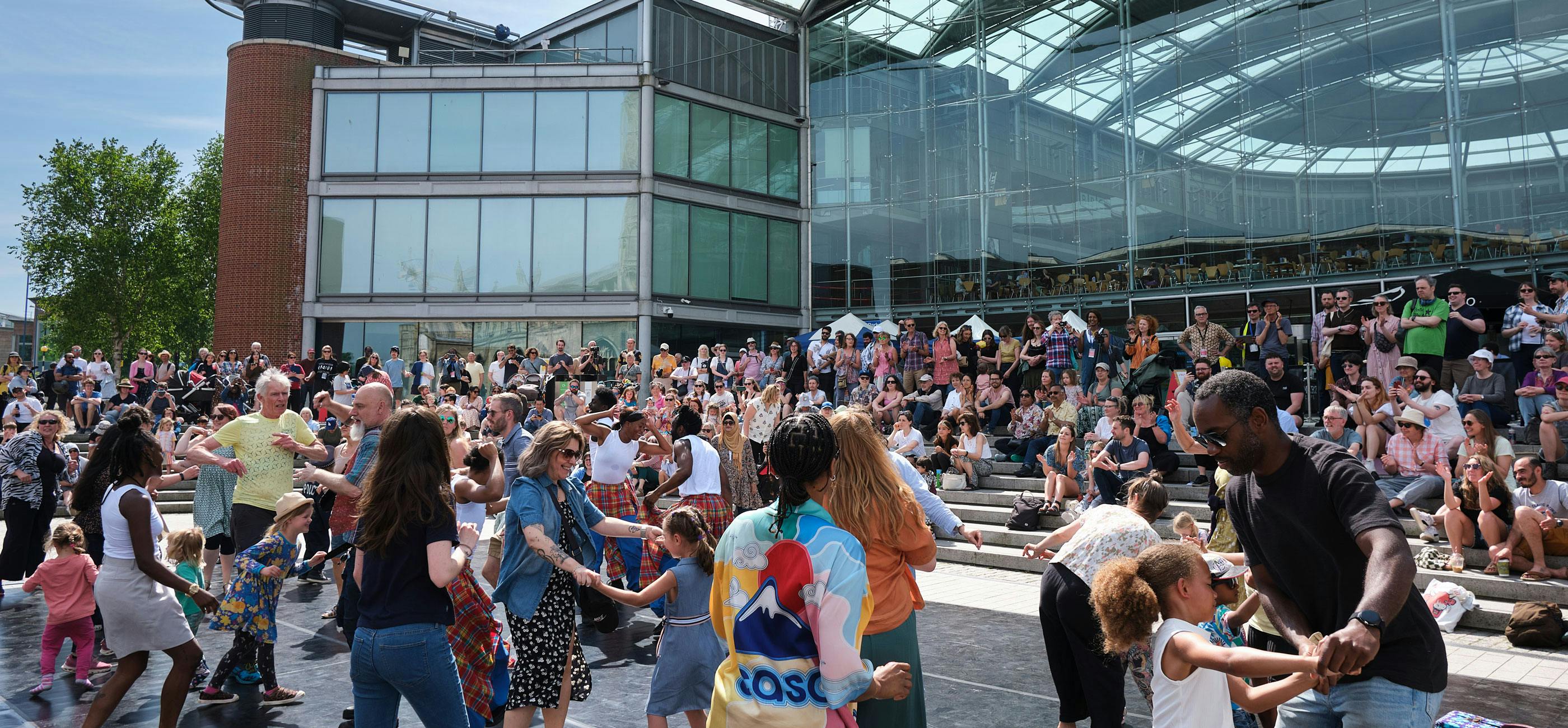 Lots of families dancing outside in The Forum in the sunshine.