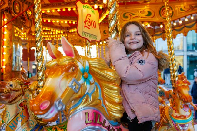 A girl smiles on a beautifully painted carousel horse