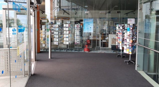 As you enter the accessible door, level grey carpeted flooring with information racks and glass lift.