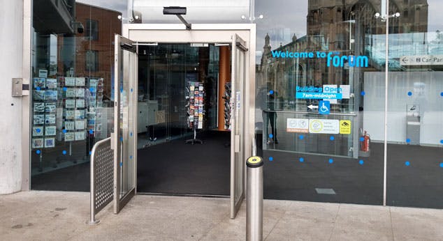 An automatic glass door at the front of The Forum, with a push button to open it on the right hand side.