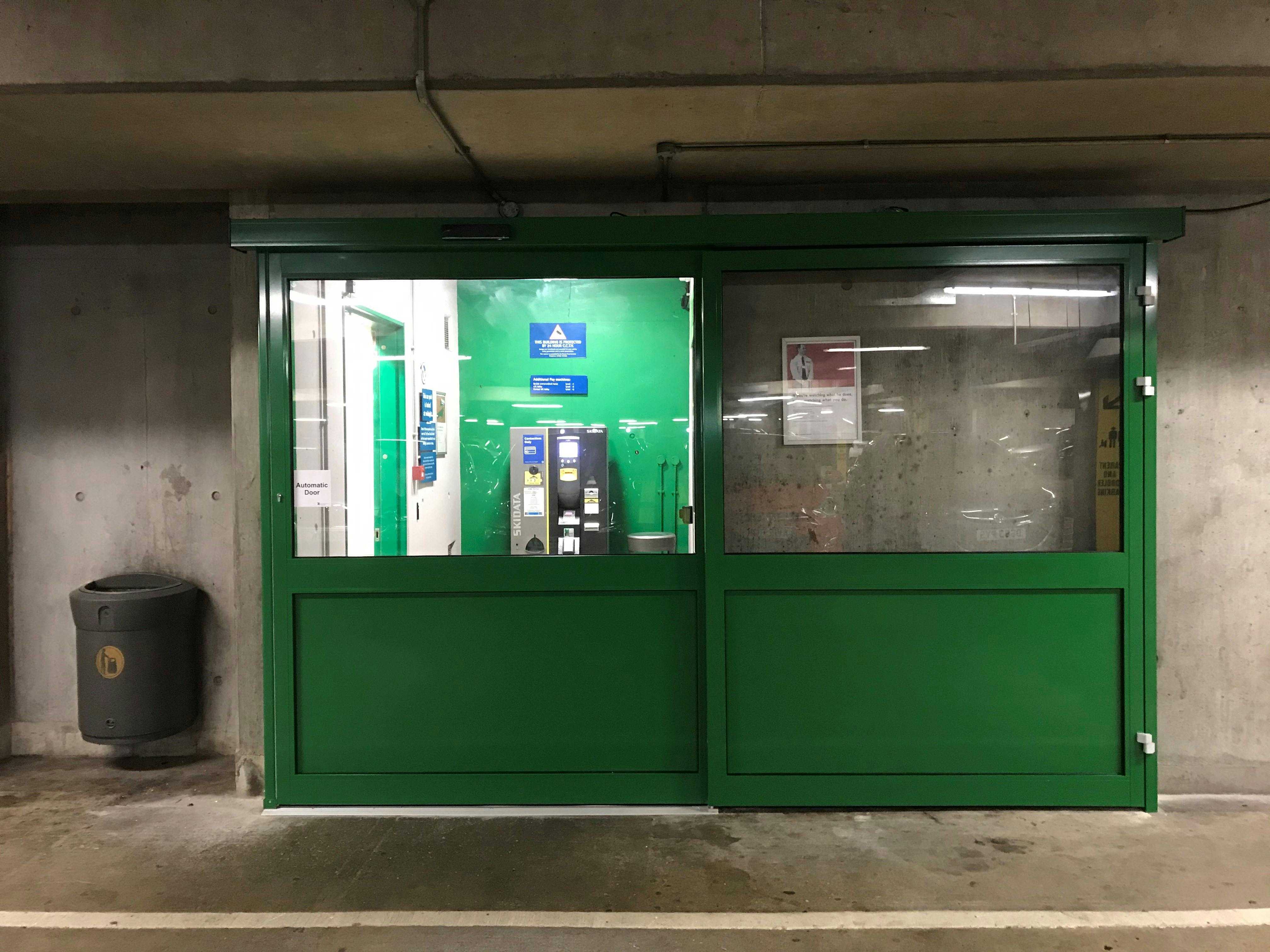 A closed green automatic door with level flooring leading to a pay machine and lift.