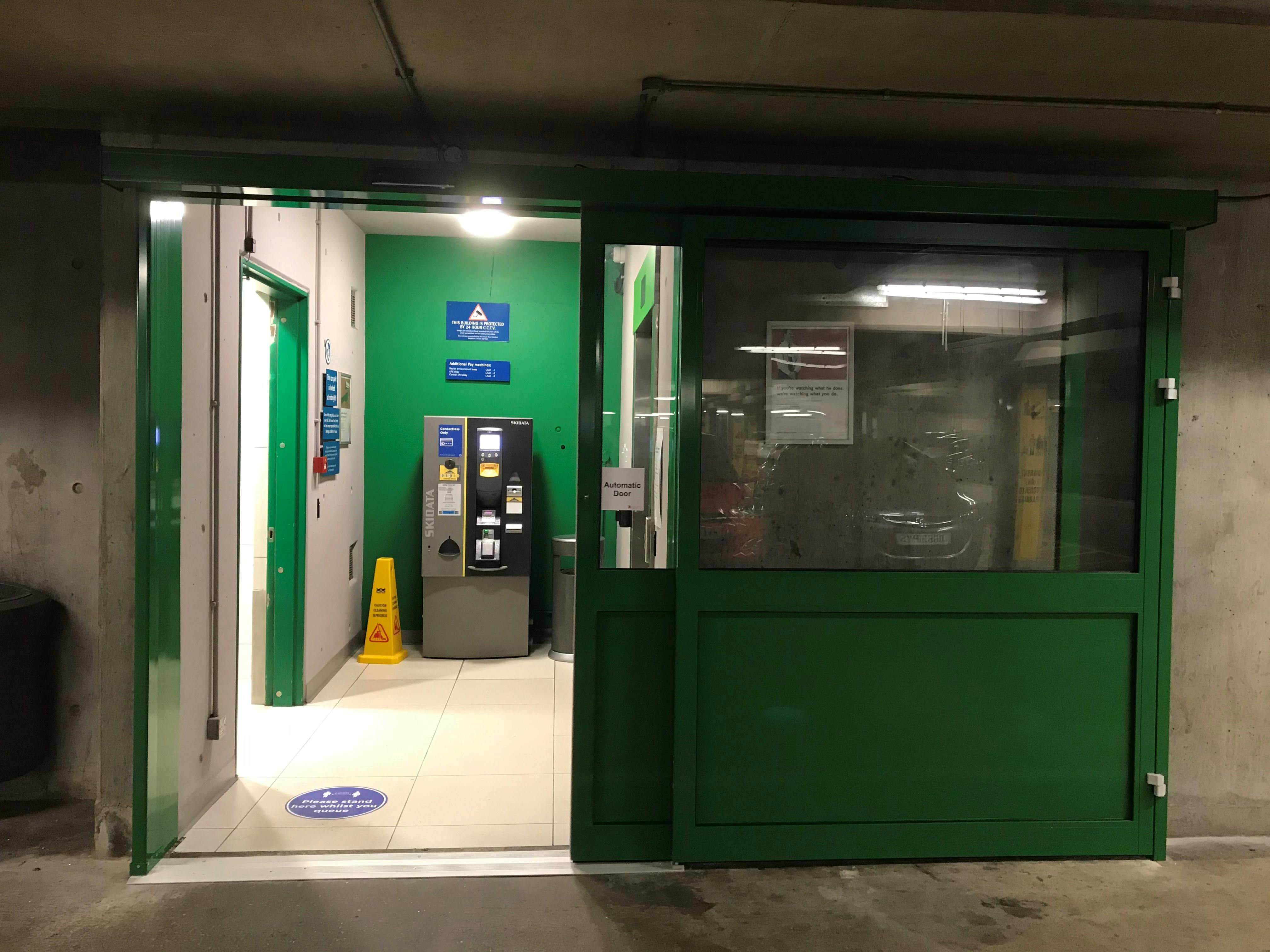 An open green automatic door with level flooring leading to a pay machine and lift.