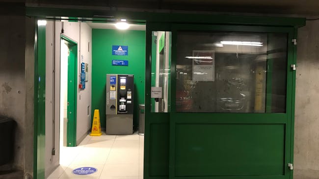 An open green automatic door with level flooring leading to a pay machine and lift.