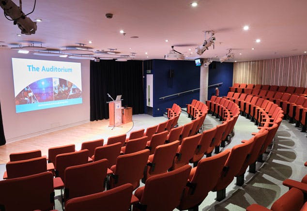 An modern auditorium space with a stage area, with podium and mic, and theatre style seating