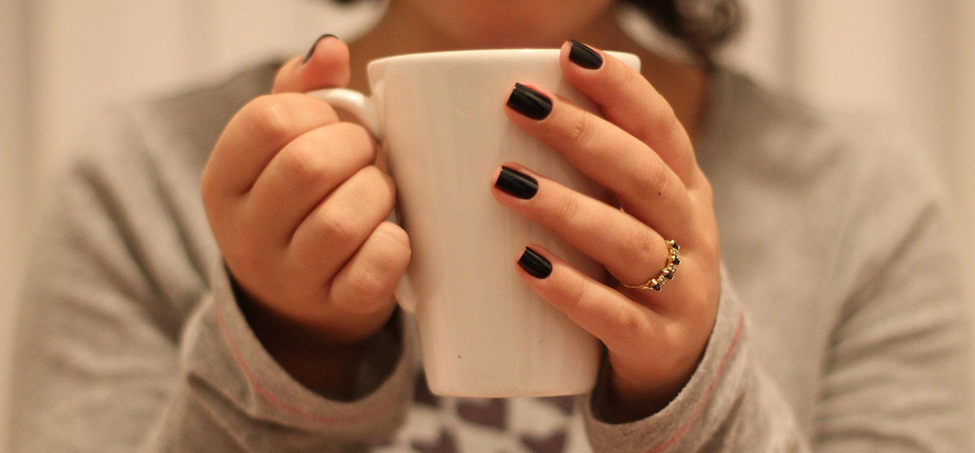 A close up of a hands holding a white mug of tea.