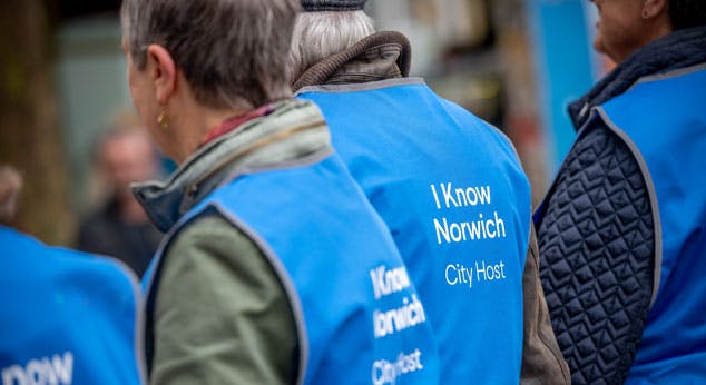 A group of people wear blue tabard with the word 'I Know Norwich, City Host' on the back.