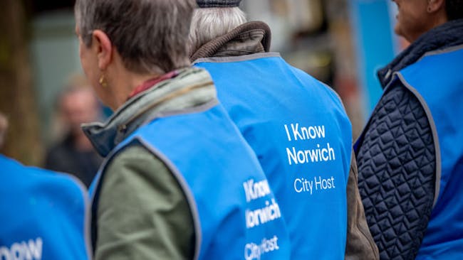 A group of people wear blue tabard with the word 'I Know Norwich, City Host' on the back.