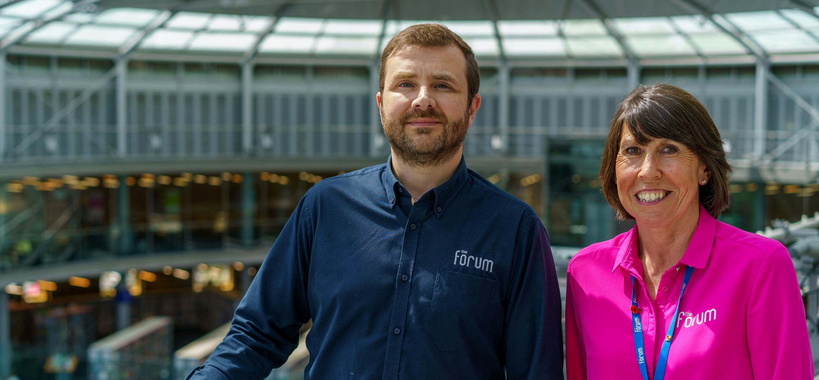 James and Kim, The Forum venue hire team, stand on the upper walkway smiling.