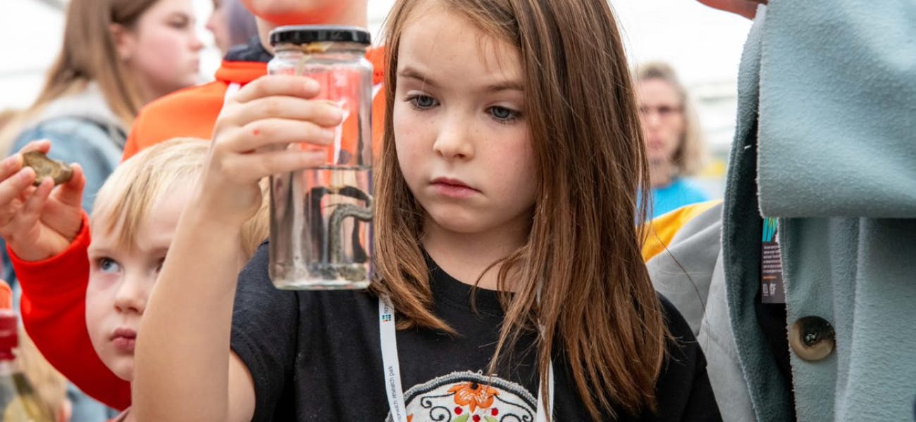 a curious child holding up a glass jar containing an amphibian in water