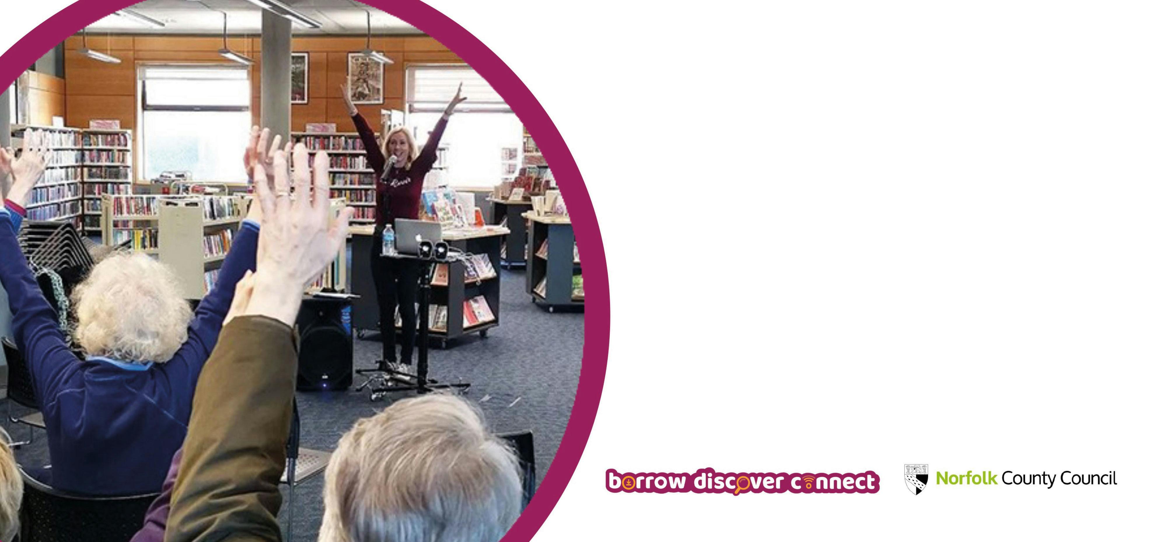 A musician sings in a library with her hands in the air, the audience are copying..
