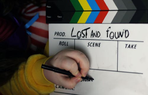 A child's hand writes on a film clapper board with the title Lost and Found on the top.