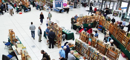 People browse a book fair with wooden shelves full with second-hand books.
