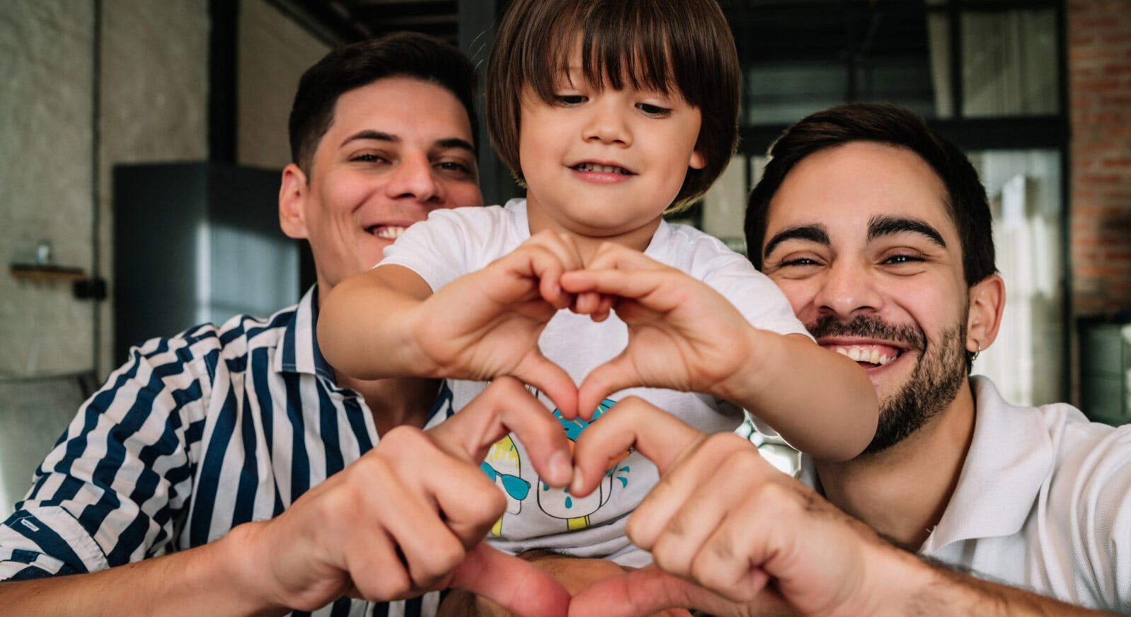 Two dads and their child make heart shapes with their hands