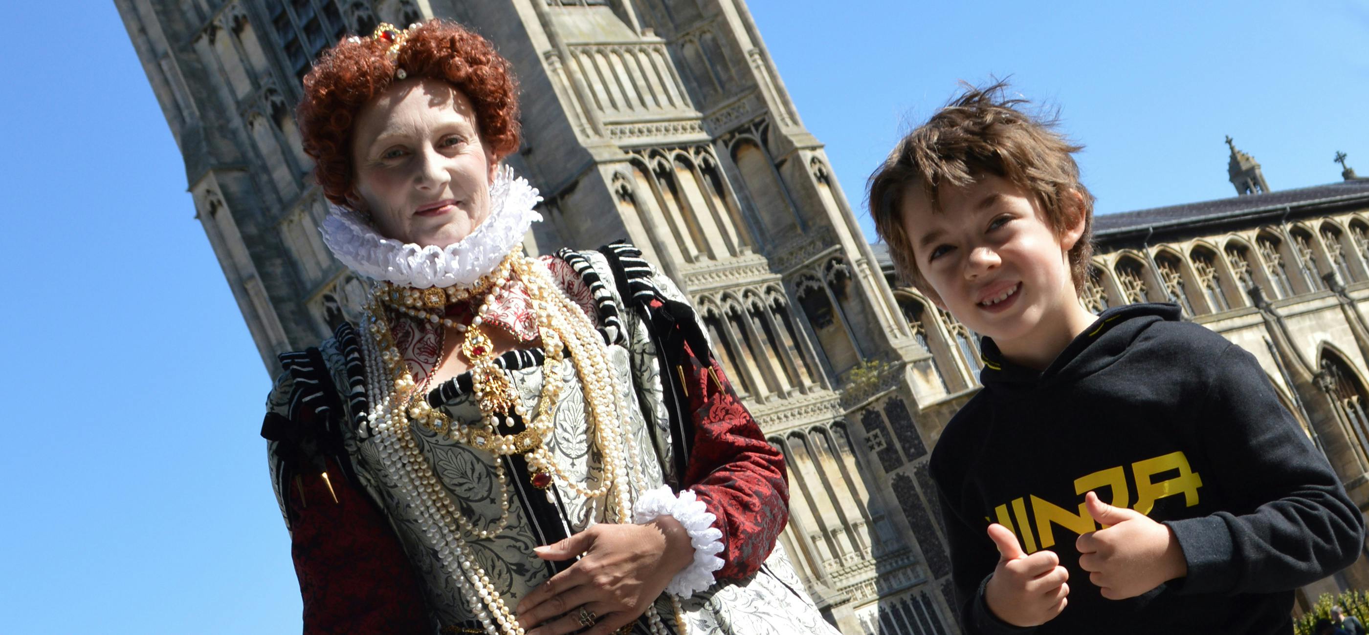 An actor dressed as Queen Victoria with ruff and pearls stands next to a child who is a history fan and has their thumbs up