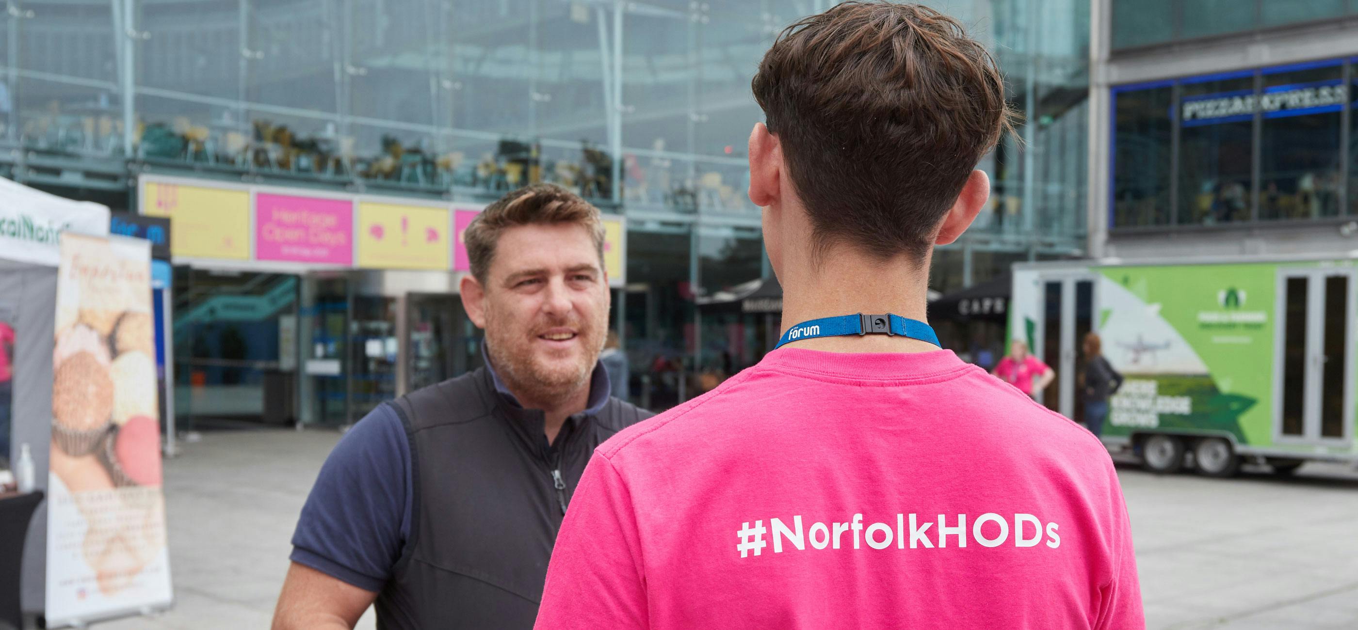 A member of the Norfolk Heritage Open Days team talks to an event organiser wearing a pink T-shirt with #NorfolkHODs on the back.