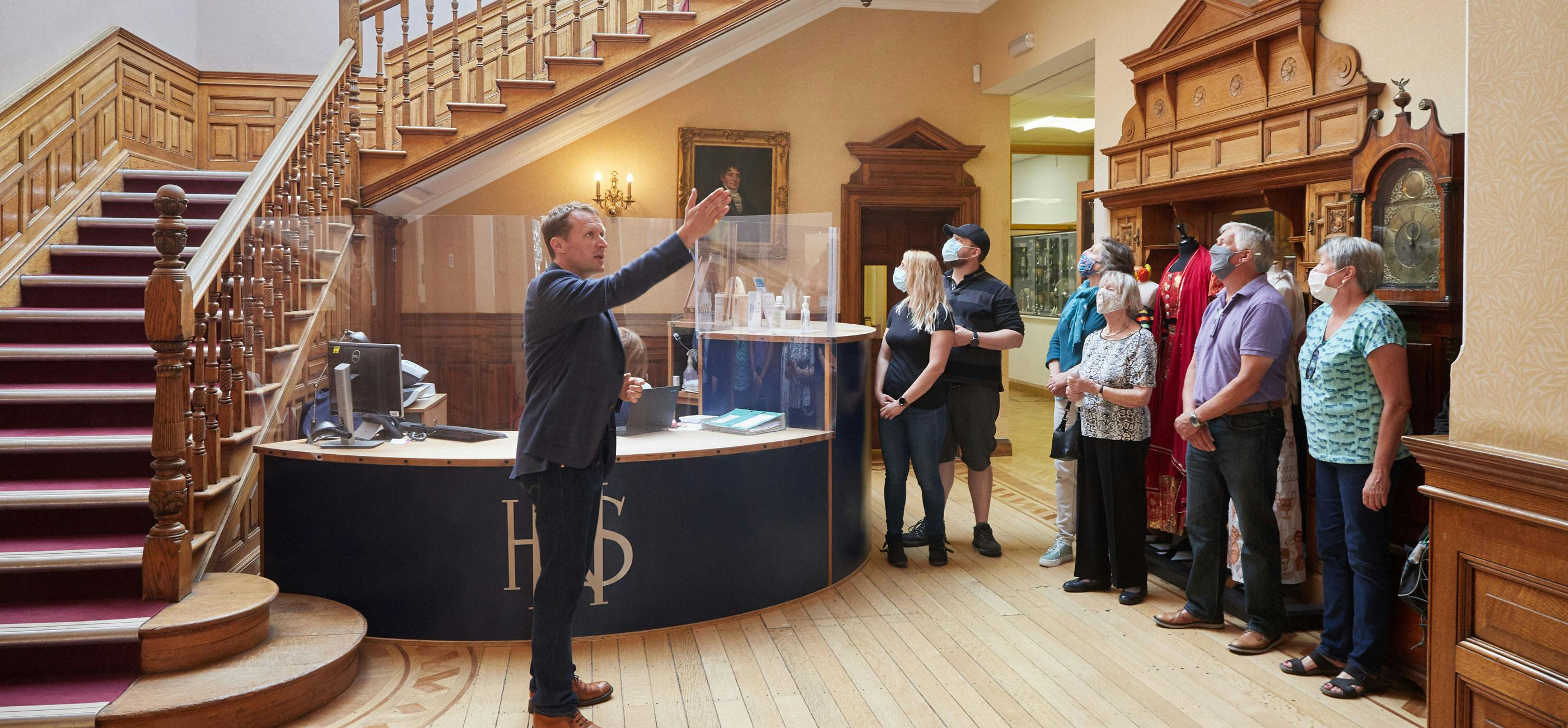 A tour guide points to a detail in a historic home with a small group of visitors.