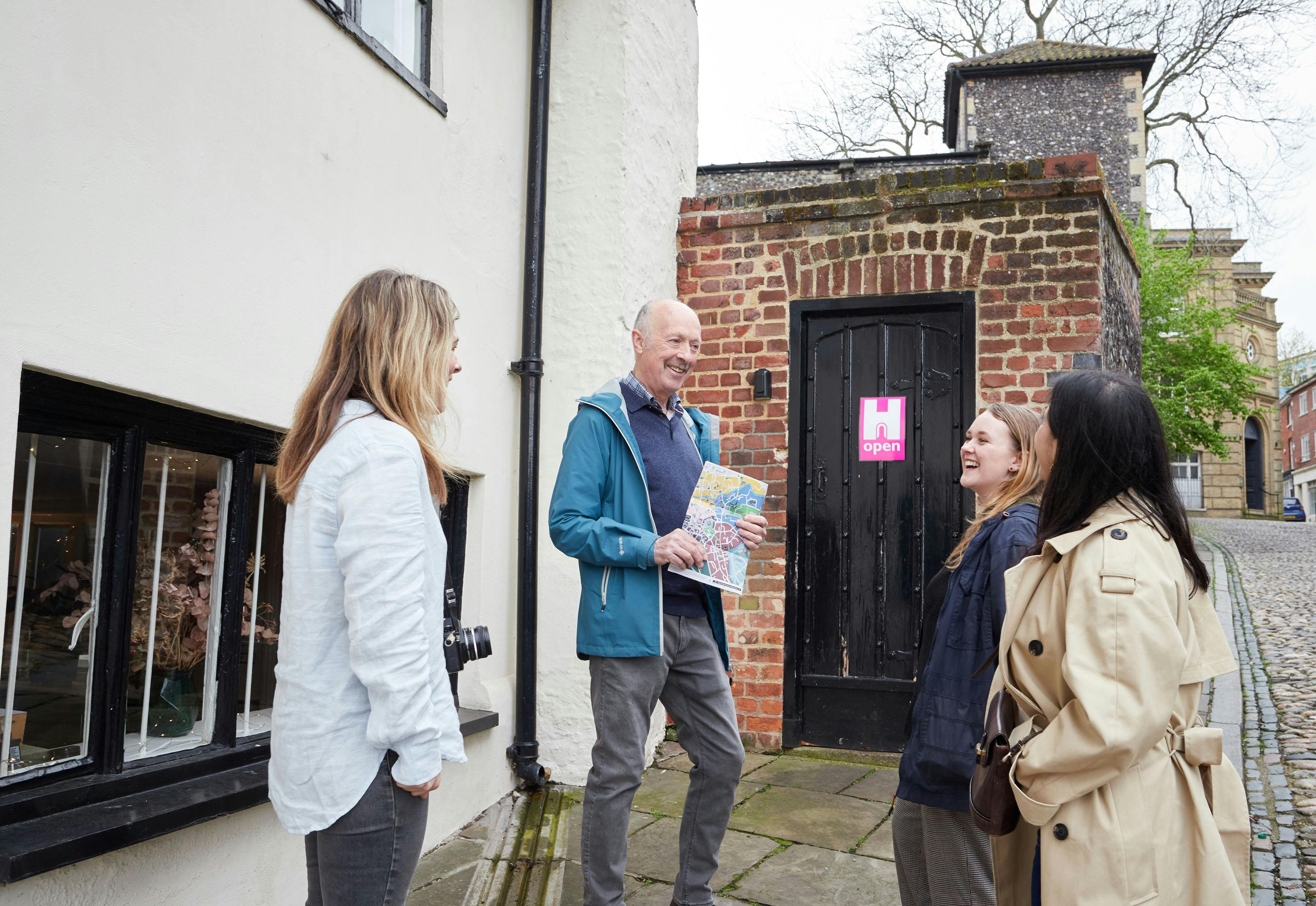 A group of women laughing as a male tour guide shares stories of Norwich