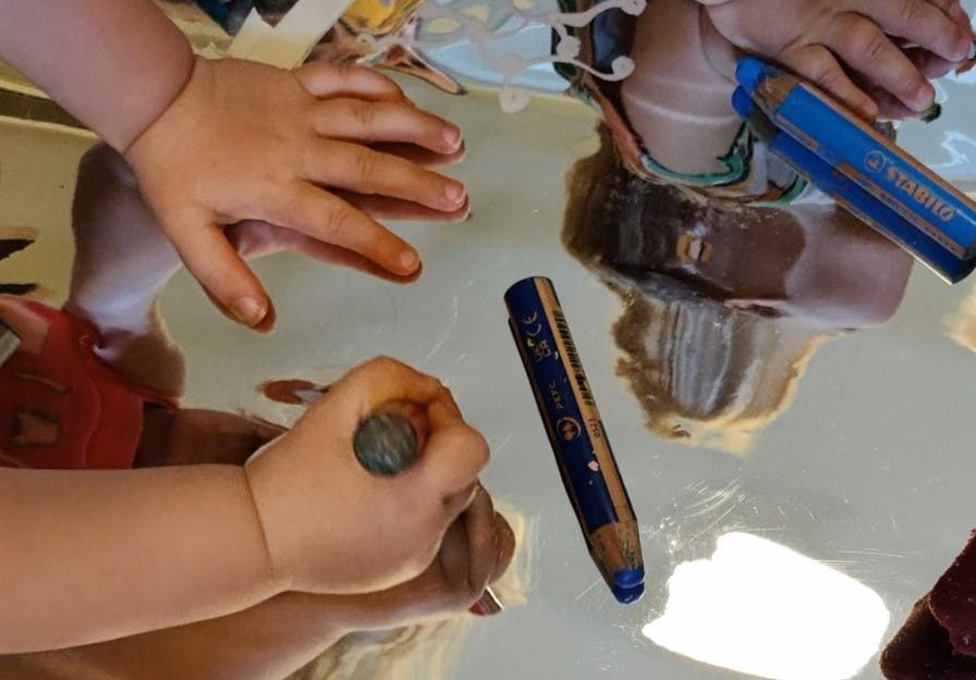 toddlers hands using a crayon drawing on a mirror
