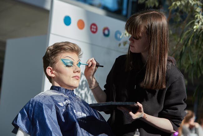 Young person having blue eye make up applied with brush