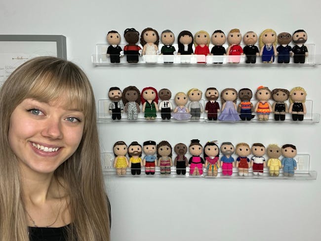 Young woman standing in front of shelf of crochet celebrity figures.