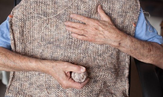 old man'shands holding an unfinished piece of knitting