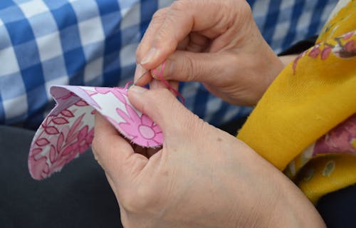 female hands using needle and thread to sew pink flowered fabric