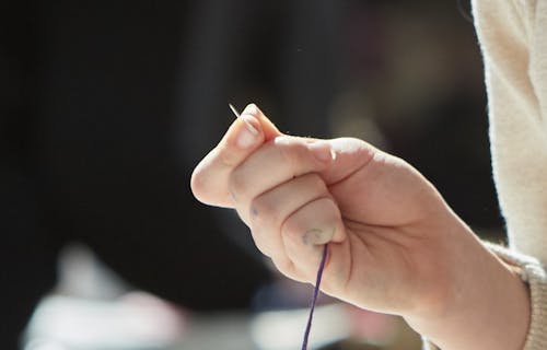 Hand holding a sewing needle and thread.