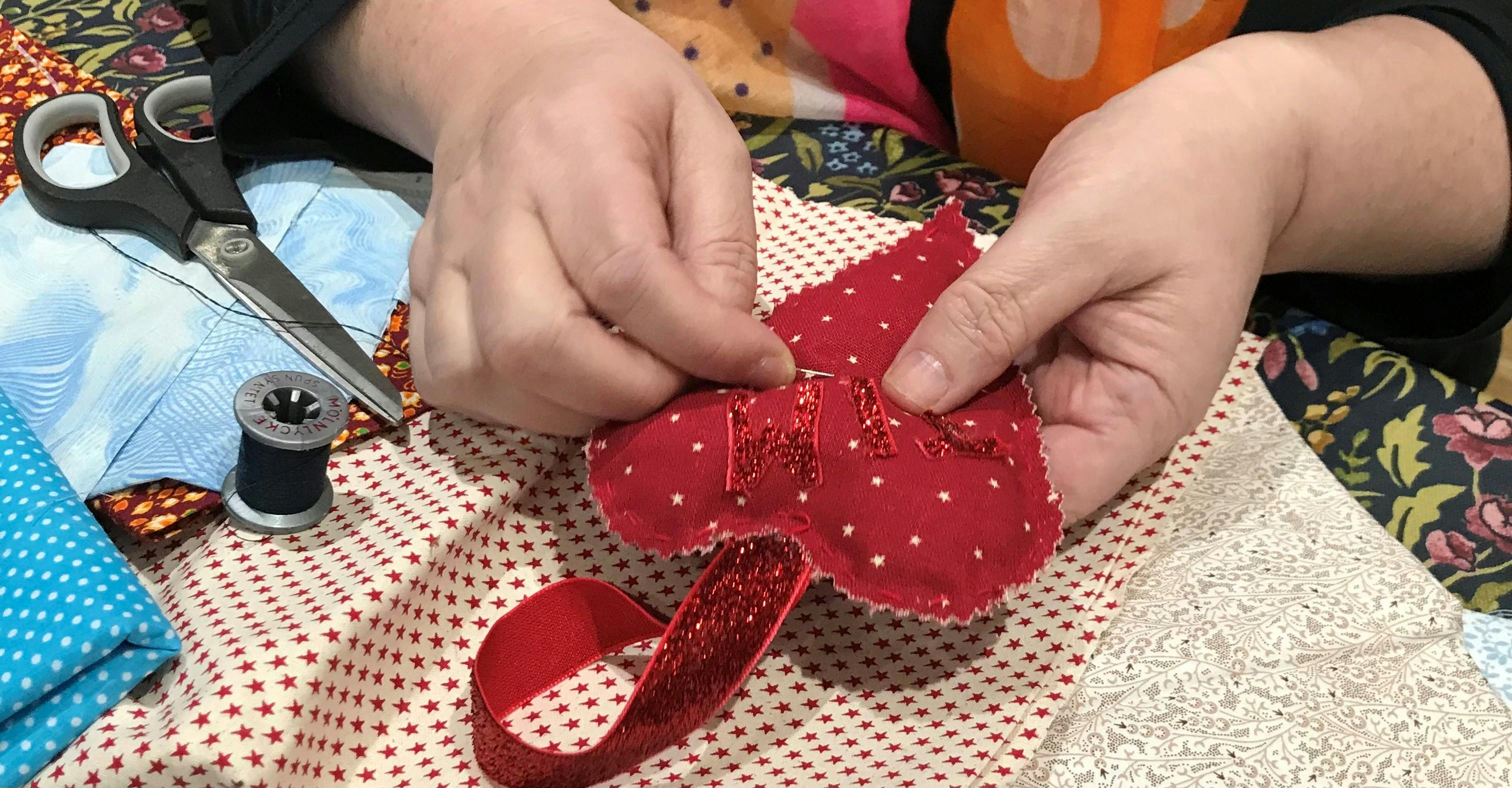 woman's hands sewing a red heart