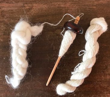 fibre, drop spindle and spun yarn laid on a wooden table