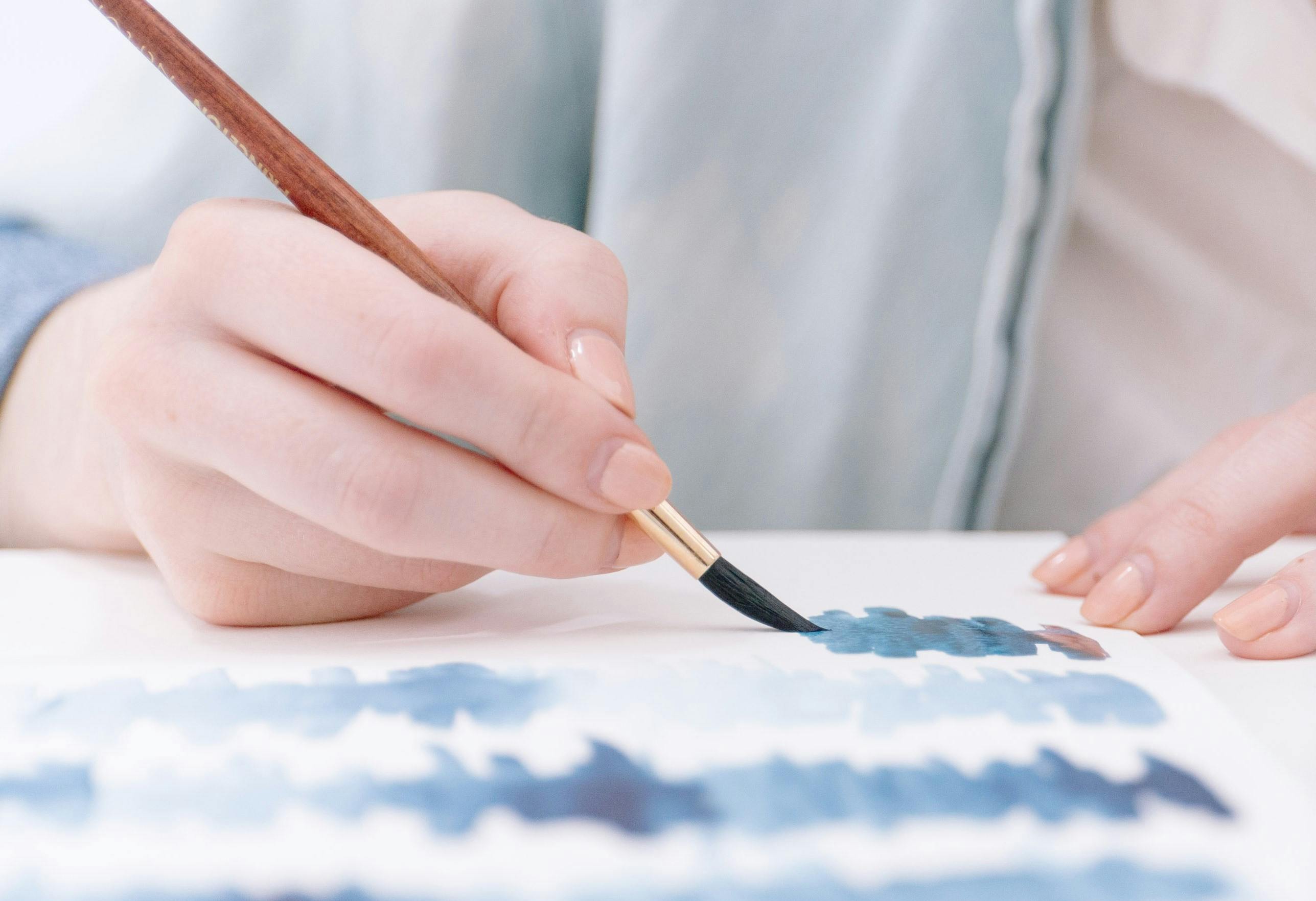 Hand painting blue shapes on a page with a watercolour paintbrush