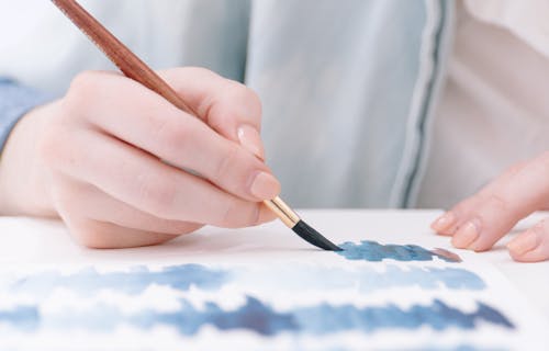Hand painting blue shapes on a page with a watercolour paintbrush