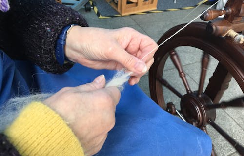hands holding fleece as it feeds into a spinning wheel