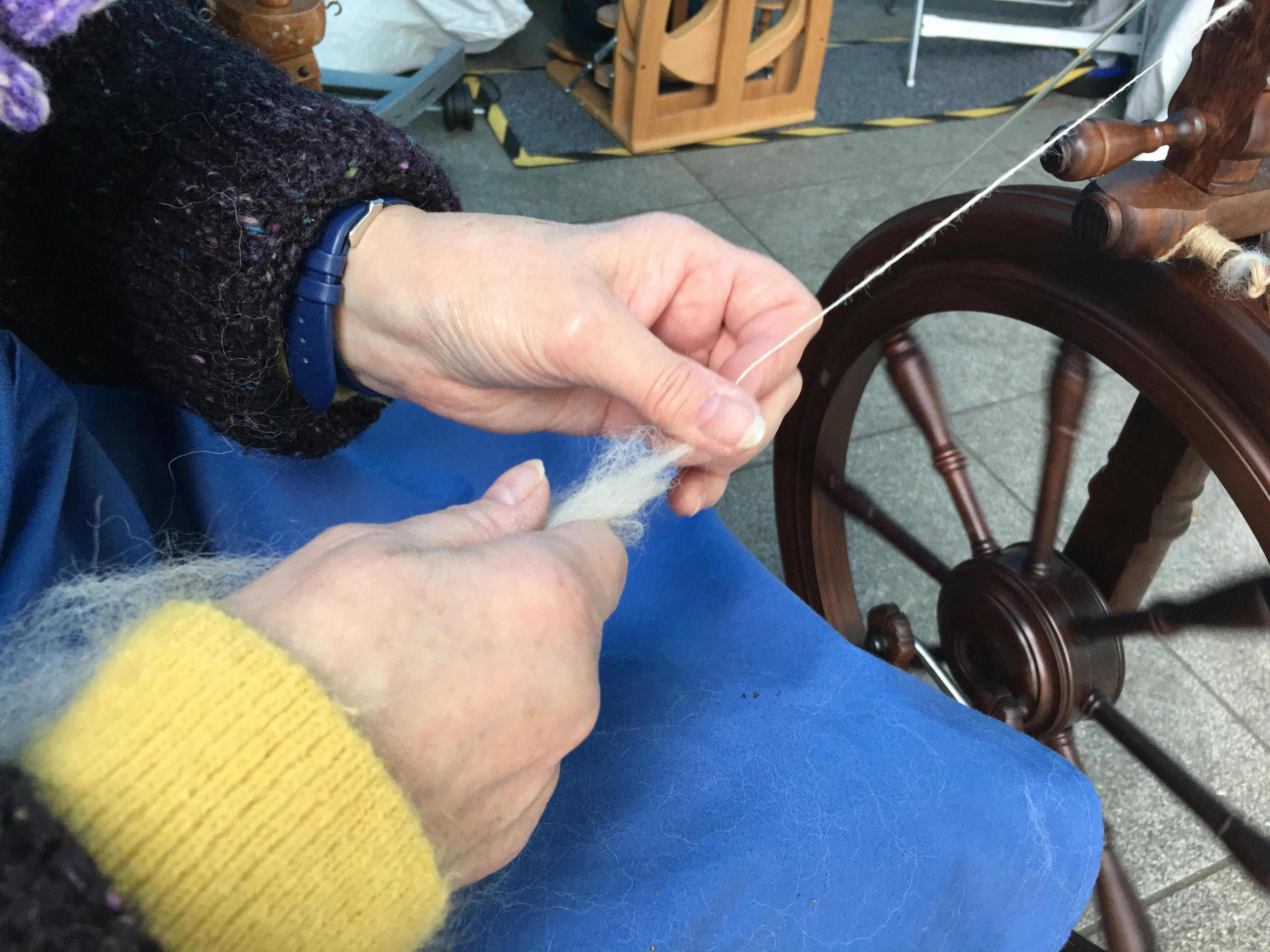 hands holding fleece as it feeds into a spinning wheel