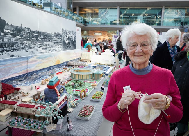 Woman knitting standing in front of knitted scene of Great Yarmouth