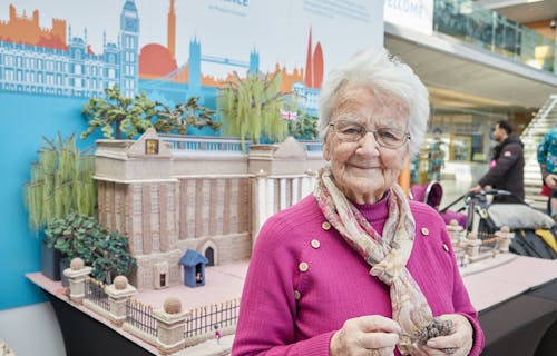 Elderly lady smiling in front of a knitted buckingham palace